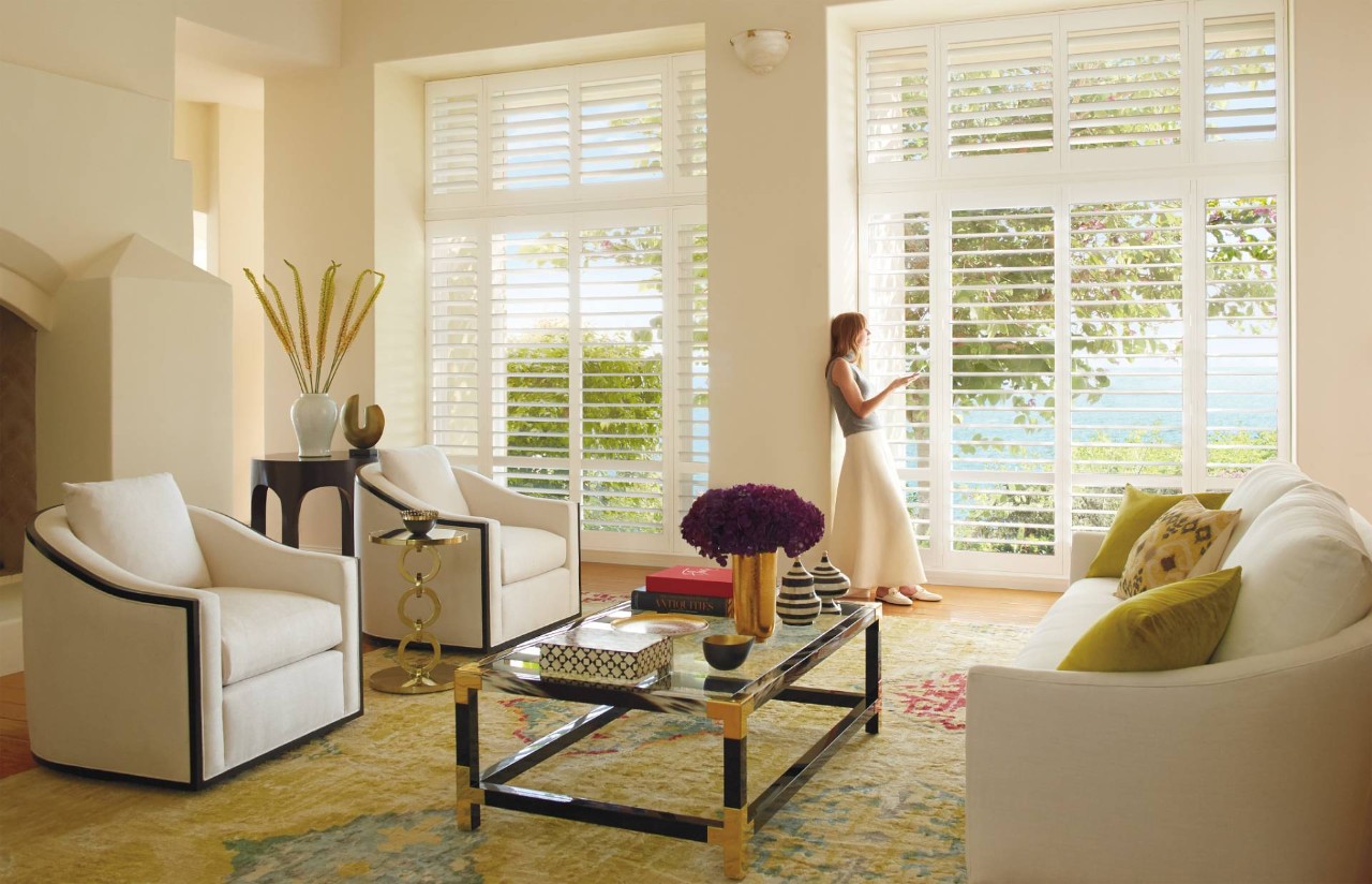 Woman standing in a traditional living room with Palm Beach® Polysatin Shutters near Newhall, CA